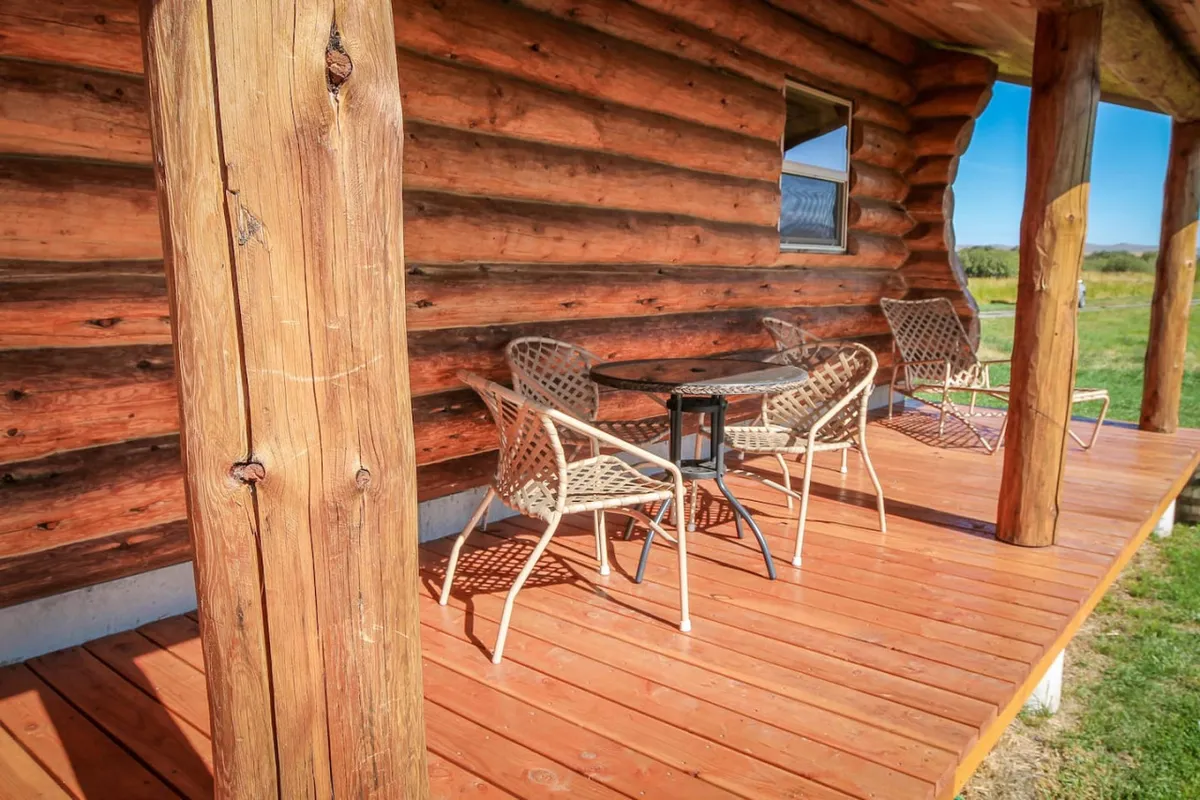 A detailed look at a porch setup with wooden log walls, a glass table, and woven chairs, all arranged for comfort and casual enjoyment. The setting is ideal for morning coffee, relaxed reading, or small gatherings—exactly the versatile use described in the section.