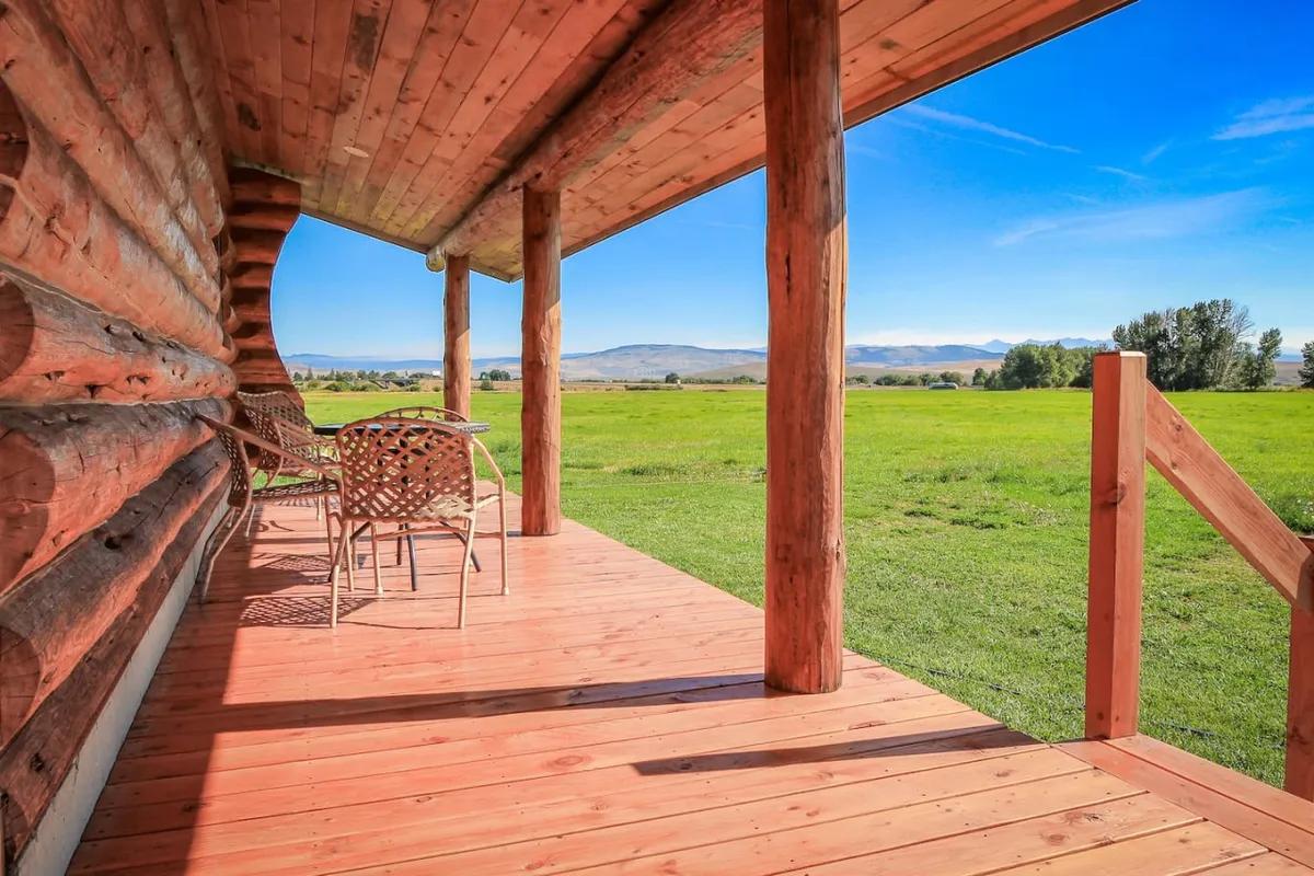 A wooden porch overlooking a lush green field with the majestic Elkhorn Mountains as a backdrop. The inviting outdoor seating area suggests a gentle transition from the restful interior to the breathtaking private views described in the section.