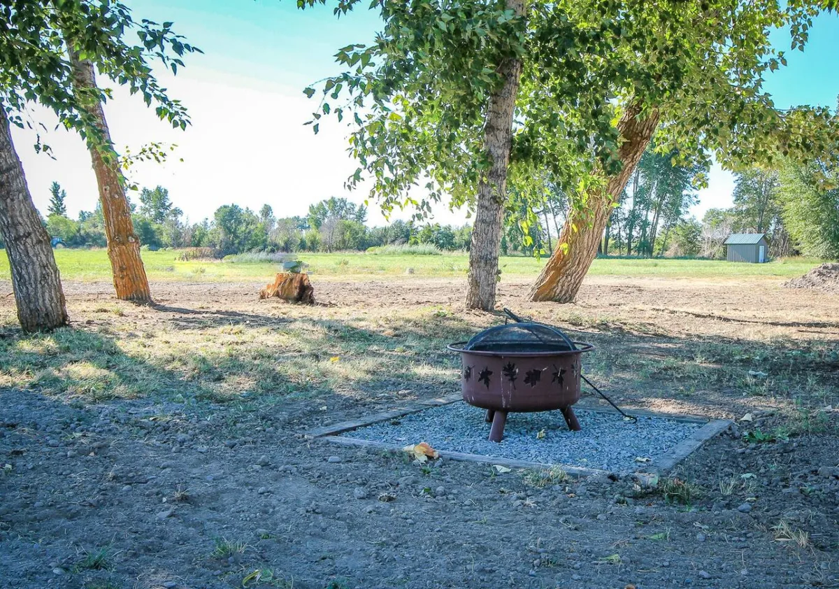 An inviting fire pit sits in an open field bordered by trees, creating a perfect setting for stargazing and campfires. The wide, unobstructed sky and natural surroundings evoke the tranquility and adventure of evenings spent outdoors after a day of exploration.