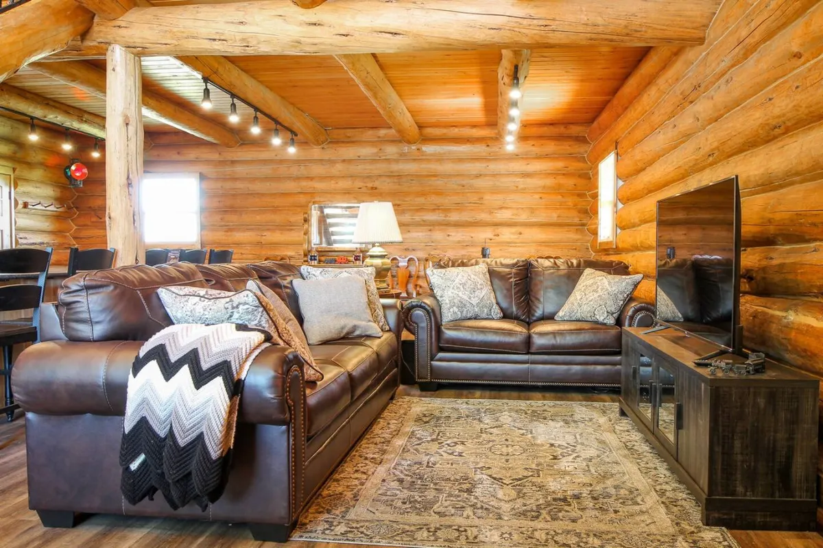 This image showcases a spacious living room featuring plush leather sofas arranged around a vibrant ornamental rug. Decorative pillows add comfort and style, while a large TV is perfectly positioned for entertainment. The room radiates warmth and invites relaxation, ideal for unwinding after a day outdoors.