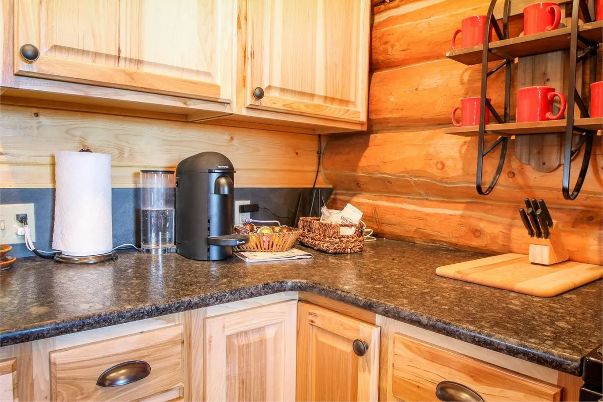 This close-up captures a corner of the kitchen featuring a coffee maker, red mugs, wooden cabinetry, and a cutting board—conjuring images of morning routines and the aroma of fresh coffee and baked goods.
