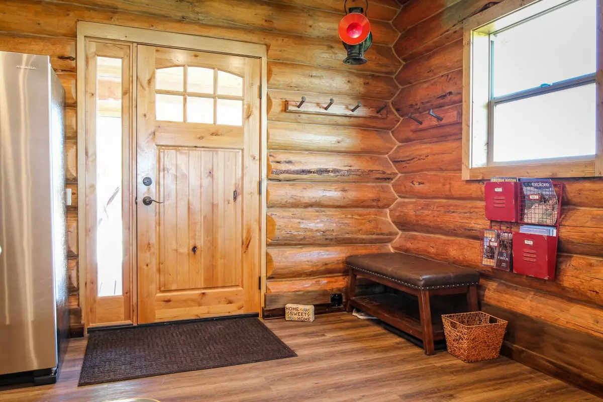 A view of the entryway with a wooden door, log walls, a bench, a metal lantern, and mail organizers. This welcoming space sets the tone for a cozy arrival and the personalized hospitality that awaits inside.