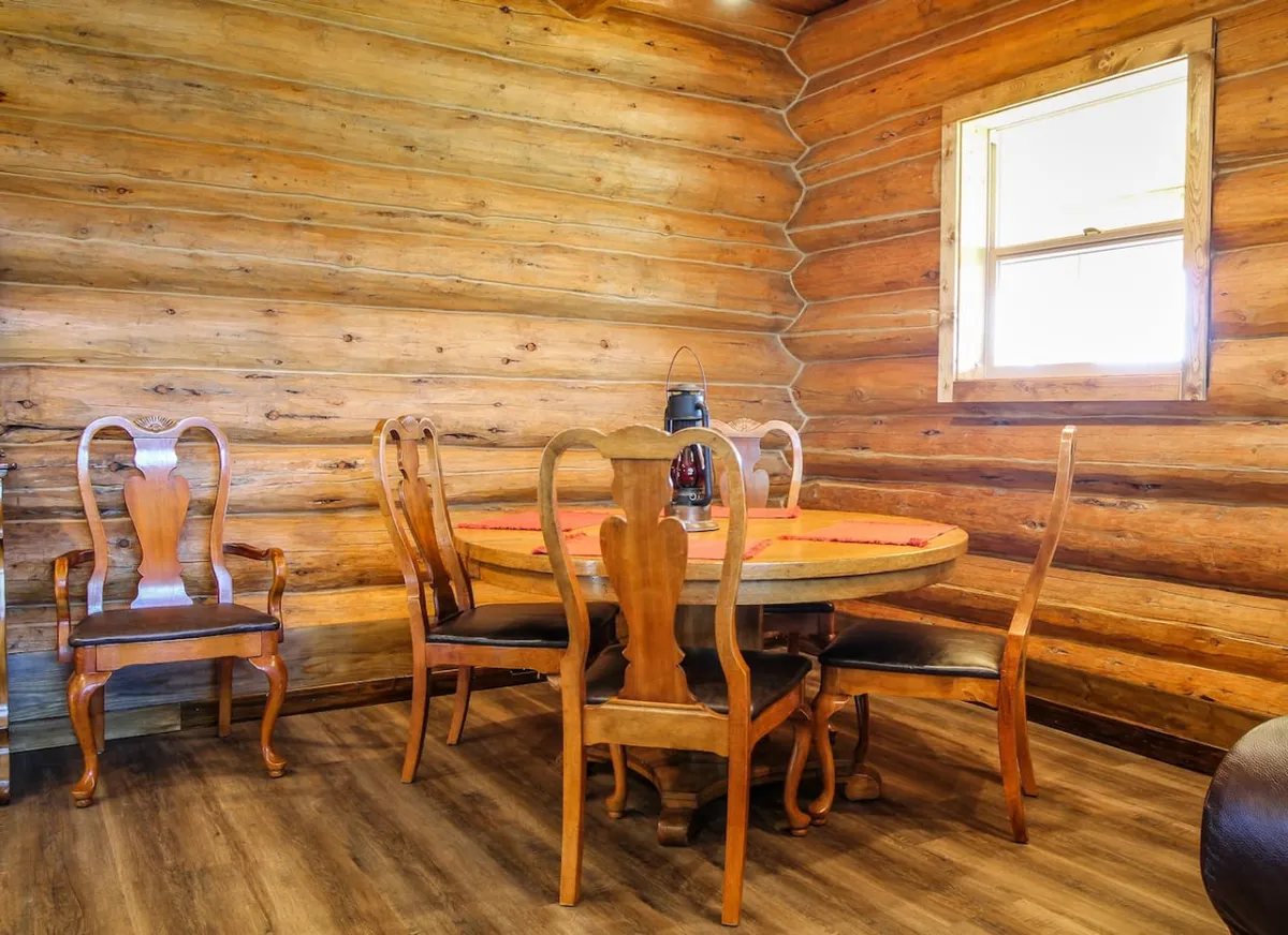 A cozy dining area with a solid wooden table surrounded by chairs and a lantern centerpiece, softly lit by natural light from a nearby window. The space feels intimate and welcoming—ideal for lingering breakfasts or romantic meals.