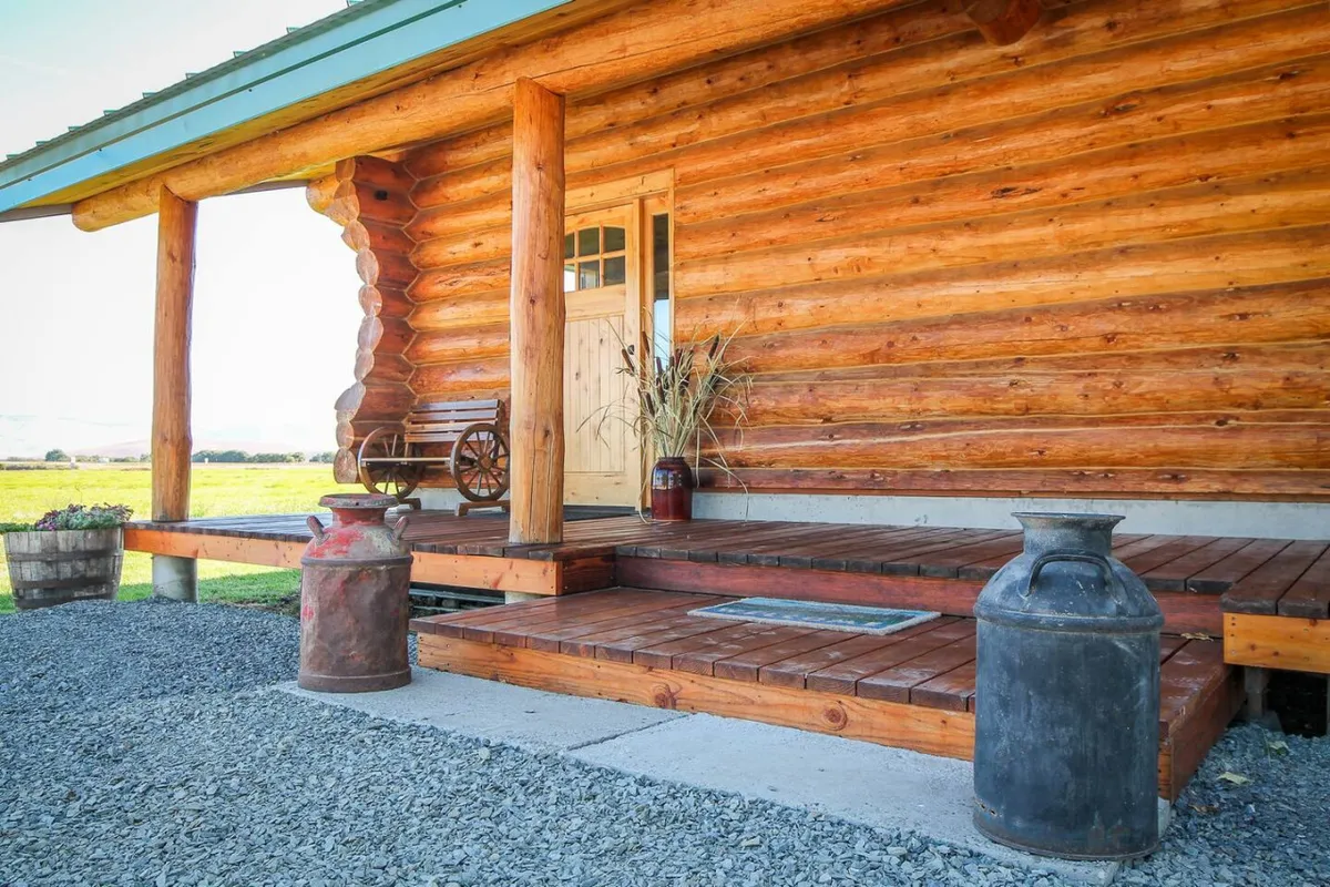 The rustic log cabin’s front porch, furnished with a classic wooden bench and decorated with milk cans, offers panoramic views of the surrounding countryside—perfect for quiet contemplation or gatherings with friends.